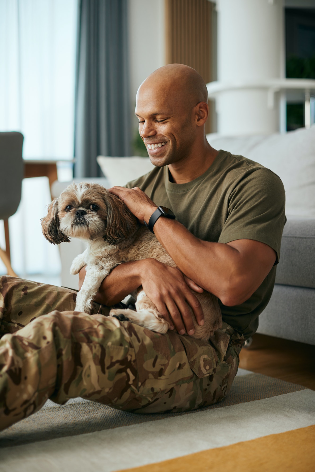 Happy black soldier cuddling his dog at home.